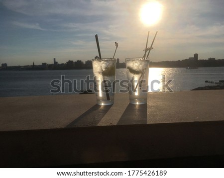 Two gin and tonics with lime and straws on the ledge of a rooftop bar in Manhattan New York City, late evening, New Jersey skyline in the background. Outdoor drinking on a rooftop.