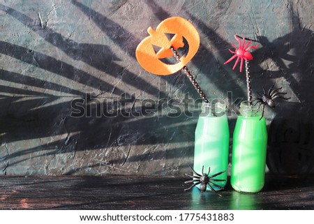  Halloween composition of green cocktail bottles, toy spiders, illumination on a black wooden table, home interior for the holiday, mystical decor