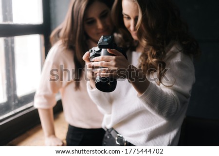 Model and female photographer looking at made photo and smiling in studio. Concept of creative work in photo studio, backstage job.