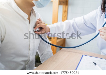 Asian Medical healthcare clinic doctor examining diagnosing male patient with stethoscope wearing surgical mask protection infection disease, working at home modern office technology computer laptop