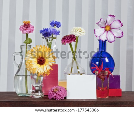 A still life of several vases and flowers with a blank card.