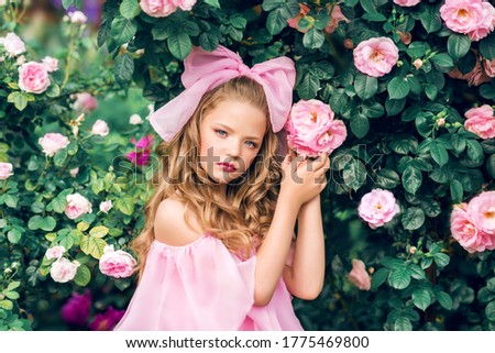 Portrait of a girl in a pink dress with a large bow among flowers. Girl doll in roses.
