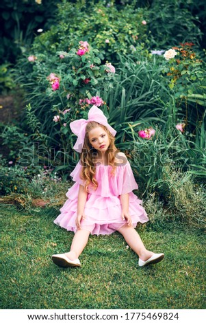 girl in a pink dress with a bow on her head in the rose garden. Girl doll