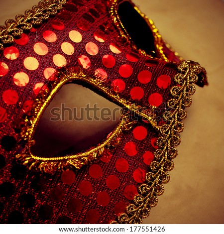 an elegant red and golden carnival mask on a brown background with a retro effect