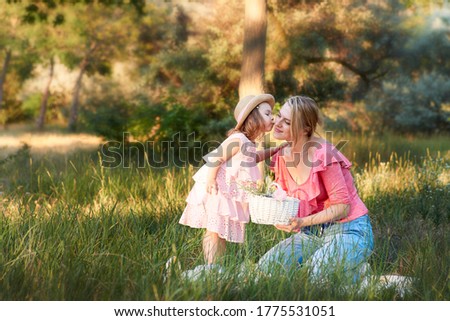 Little girl kissing mother sitting on green grass outdoors in park Happy family Summer time