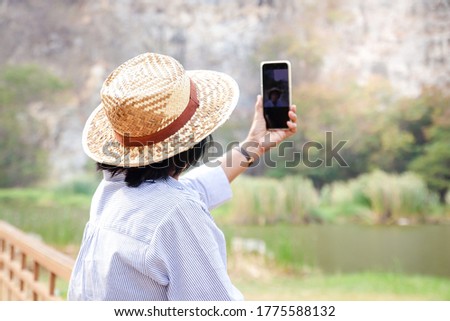Asian senior woman Holding a smartphone, taking a picture and playing social media, she enjoys her retirement life. Elderly community concept.