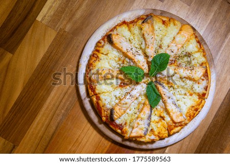 Original Italian seafood pizza. Original recipe. Cutted pizza with potato, smoked salmon, cream and leaves on wooden table. True and authentic.