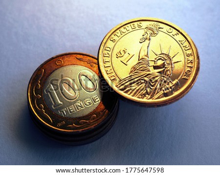 Kazakh coin in 100 tenge and American one dollar. News about exchange rate and the economy of Kazakhstan. A dramatic dark gloomy illustration with enhanced contrast and saturation. Macro