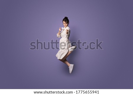 Serious caucasian woman jumping on a violet studio wall with free space and pointing at camera