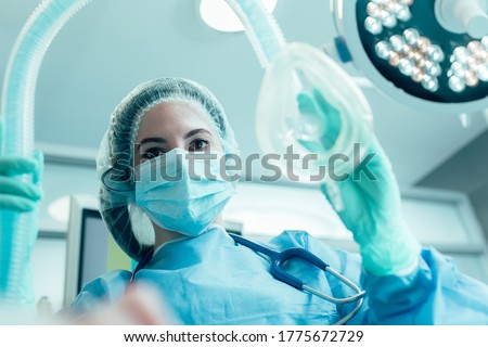 Doctor in medical mask and protective clothes standing with an anesthesia mask in her hand Royalty-Free Stock Photo #1775672729