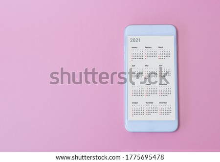  White smart phone show calendar App 2021 on pink background. New Year Concept. Royalty-Free Stock Photo #1775695478