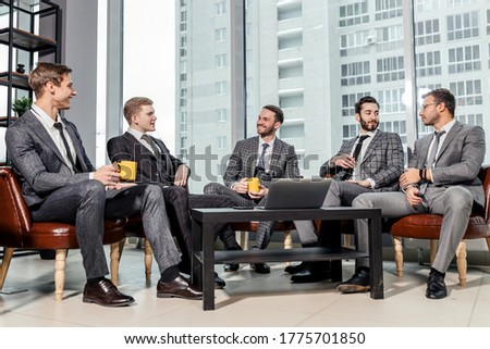 leisure time of business team consisted of young men in suits, talking over a cup of tea together in office, successful partnership of happy male in modern office