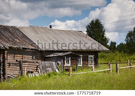 Traditional village house on a background of summer landscape of grass and blue sky and fences during the day. Old northern residential architecture of Russia. Log dwelling is called izba