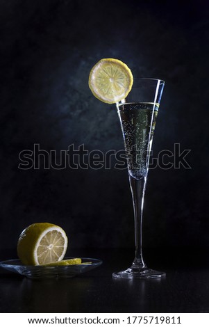 Bright glass with champagne and lemon on a dark background. Christmas and New Year design. Dark mode. Photo for banners and posters. The concept of sales, Christmas gifts and shopping.