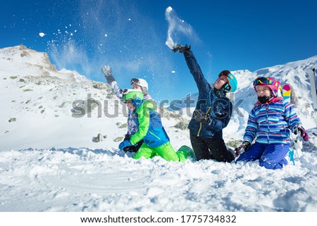 Group of kids play in snow throwing snowballs in ski outfit playing fun game together