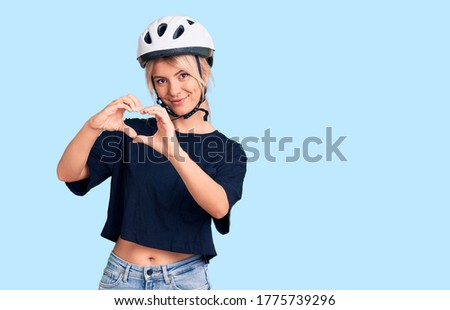 Young beautiful blonde woman wearing bike helmet smiling in love showing heart symbol and shape with hands. romantic concept. 