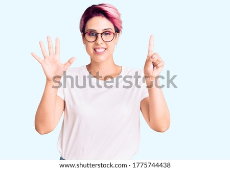 Young beautiful woman with pink hair wearing casual clothes and glasses showing and pointing up with fingers number six while smiling confident and happy. 