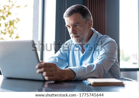 Mature businessman working on laptop. Handsome mature business leader sitting in a modern office Royalty-Free Stock Photo #1775745644