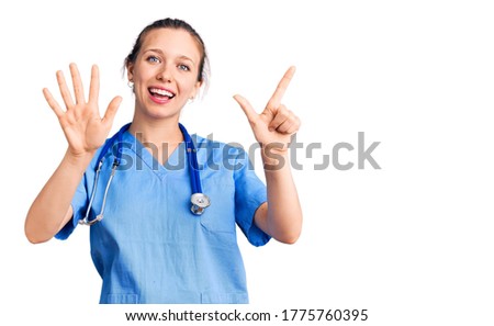 Young beautiful blonde woman wearing doctor uniform and stethoscope showing and pointing up with fingers number seven while smiling confident and happy. 