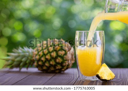 fresh pineapple juice pouring into glass on wooden table outdoors