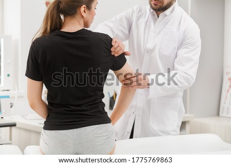 Male doctor examining female patient suffering from elbow pain. Medical exam. Chiropractic, osteopathy, post traumatic rehabilitation,sport physical therapy. Alternative medicine, pain relief concept. Royalty-Free Stock Photo #1775769863