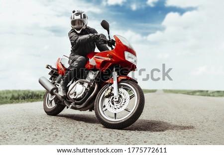 A man rides a motorcycle on the highway to the camera. A man on a red motorcycle makes a turn in front of the camera Royalty-Free Stock Photo #1775772611