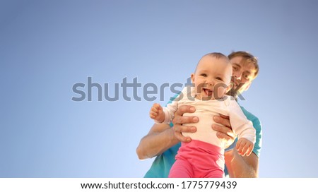 Father holds a small child in his arms on a background of a summer blue sky. Cute baby is smiling. Happy family outdoors. Right space for text.