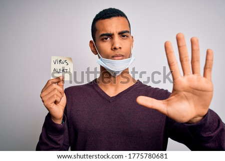 Young handsome african american man wearing medical mask holding virus alert reminder with open hand doing stop sign with serious and confident expression, defense gesture
