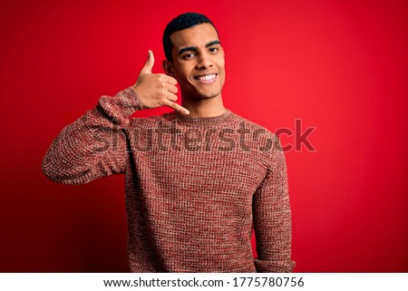 Young handsome african american man wearing casual sweater standing over red background smiling doing phone gesture with hand and fingers like talking on the telephone. Communicating concepts.