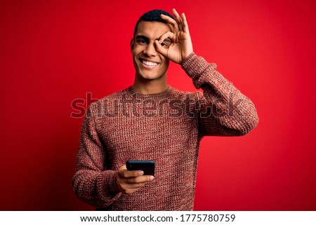 Handsome african american man having conversation using smartphone over red background with happy face smiling doing ok sign with hand on eye looking through fingers