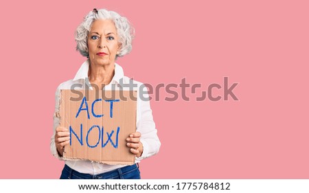 Senior grey-haired woman holding act now banner thinking attitude and sober expression looking self confident 