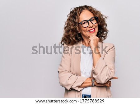 Middle age beautiful businesswoman wearing glasses standing over isolated white background smiling looking confident at the camera with crossed arms and hand on chin. Thinking positive.