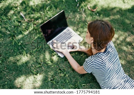 A woman in a park lies on the grass in front of a laptop learning online lifestyle work