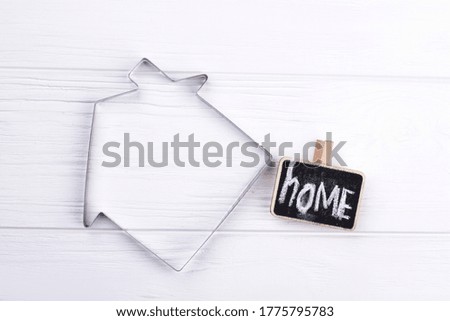 Dreaming about own house and home. Metallic frame of house and small chalkboard on white background.