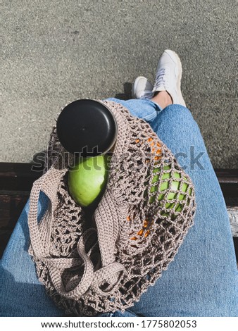 Reusable eco-friendly mesh bag with apples and water on the girl's lap. Photo from the top