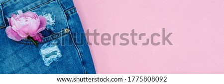 Torn denim jeans with pink peony flower on pink background. Ripped blue trousers and bloom. Trendy fashion design, top view, copy space, banner.