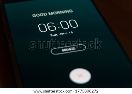 On a black smartphone, an alarm clock rings for 6 am with the inscription Good morning close-up, background