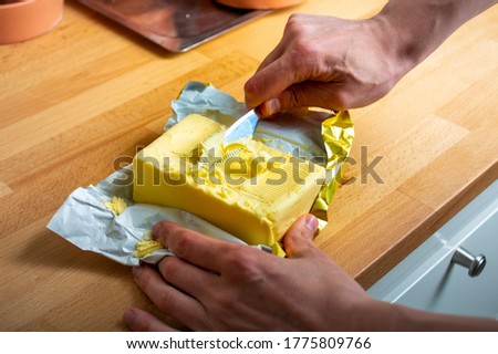 Cutting butter for a sandwich. Male hand holding a knife, block of butter on a kitchen table. Royalty-Free Stock Photo #1775809766
