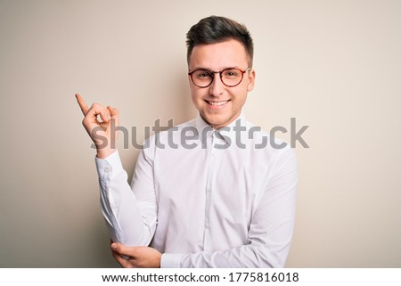 Young handsome business mas wearing glasses and elegant shirt over isolated background with a big smile on face, pointing with hand and finger to the side looking at the camera.