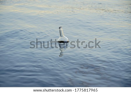 An empty glass wine bottle floats on the water. It is carried by the river