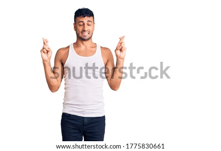 Young hispanic man wearing casual clothes gesturing finger crossed smiling with hope and eyes closed. luck and superstitious concept. 