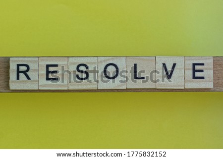gray word resolve in small square wooden letters with black font on a yellow background