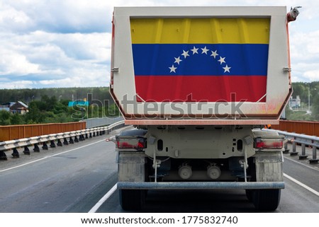 Big  truck with the national flag of  Venezuela moving on the highway, against the background of the village and forest landscape. Concept of export-import,transportation, national delivery of goods 