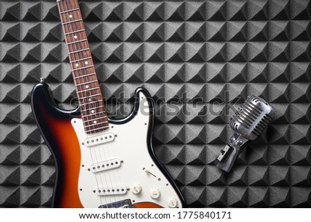 Electric guitar and retro microphone on acoustic foam panel background