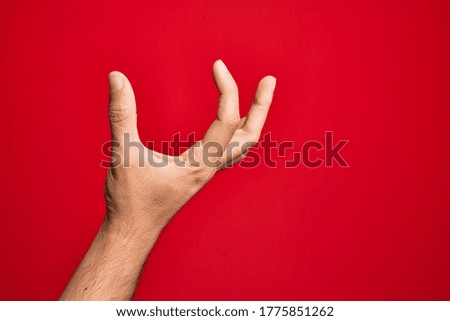 Hand of caucasian young man showing fingers over isolated red background picking and taking invisible thing, holding object with fingers showing space