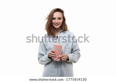 A young girl in a denim shirt eats popcorn on a white background. American-style