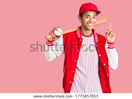 Young african amercian man playing baseball holding bat and ball surprised with an idea or question pointing finger with happy face, number one 