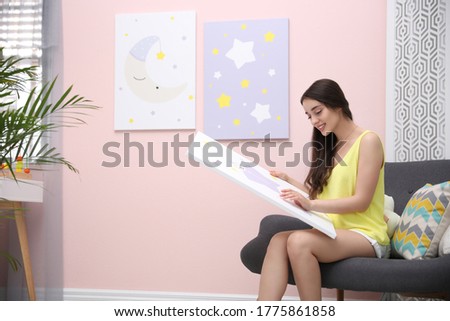 Decorator with picture sitting near pink wall indoors. Children's room interior design