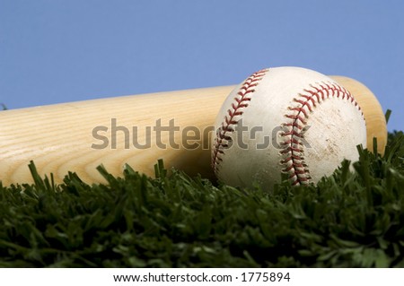 Baseball laying on grass with bat against blue sky