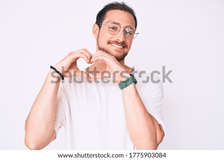 Young handsome man wearing casual clothes and glasses smiling in love doing heart symbol shape with hands. romantic concept. 